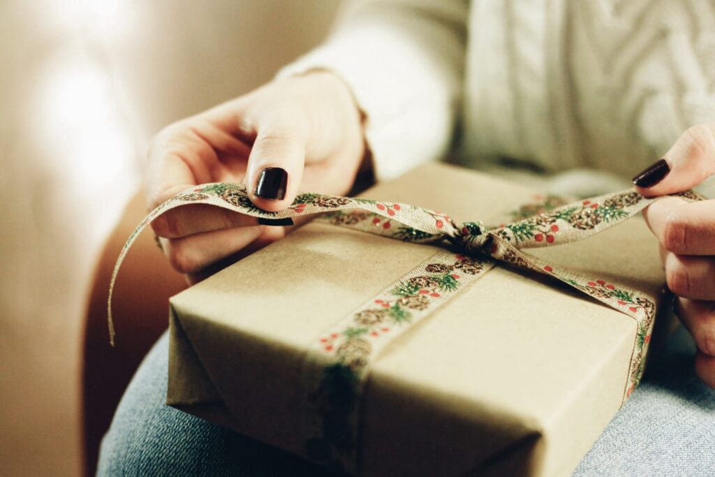 Close-up of a person opening a present wrapped in brown paper and holiday ribbon
